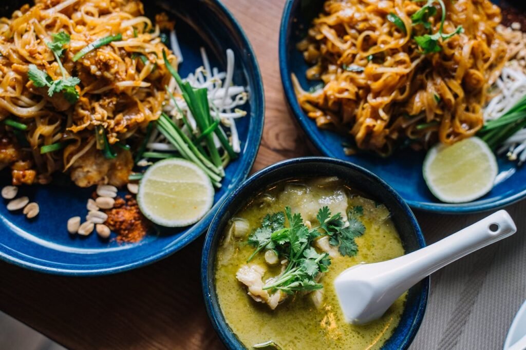 Close-up of delicious Asian noodles and creamy green curry, garnished with fresh herbs.