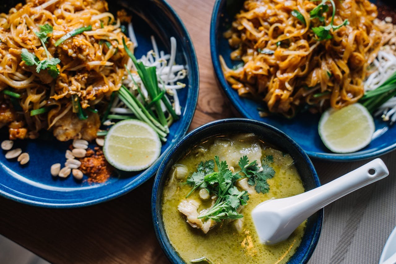 Close-up of delicious Asian noodles and creamy green curry, garnished with fresh herbs.